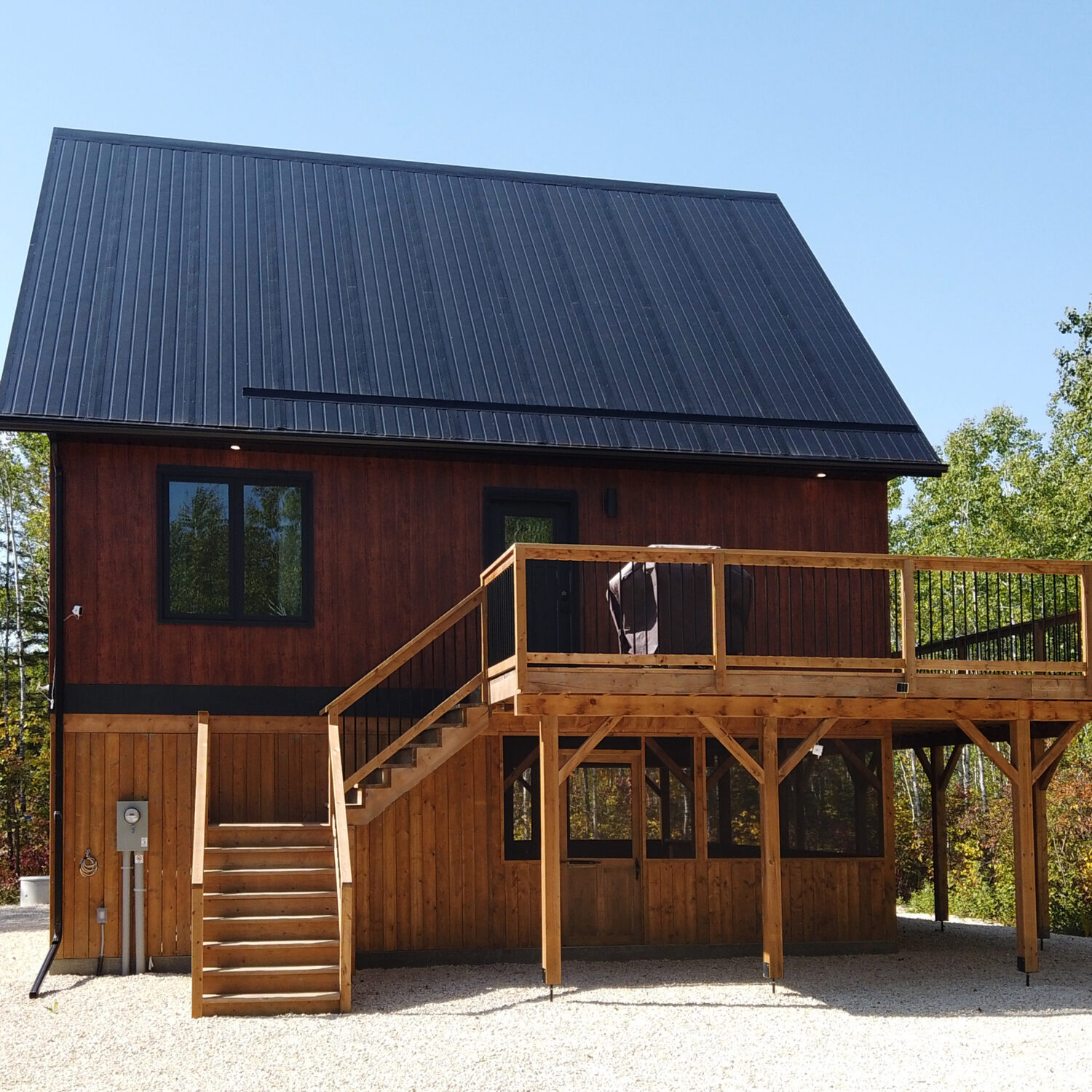 Cabin on stilts with wrap-around deck amongst trees with black steel roof