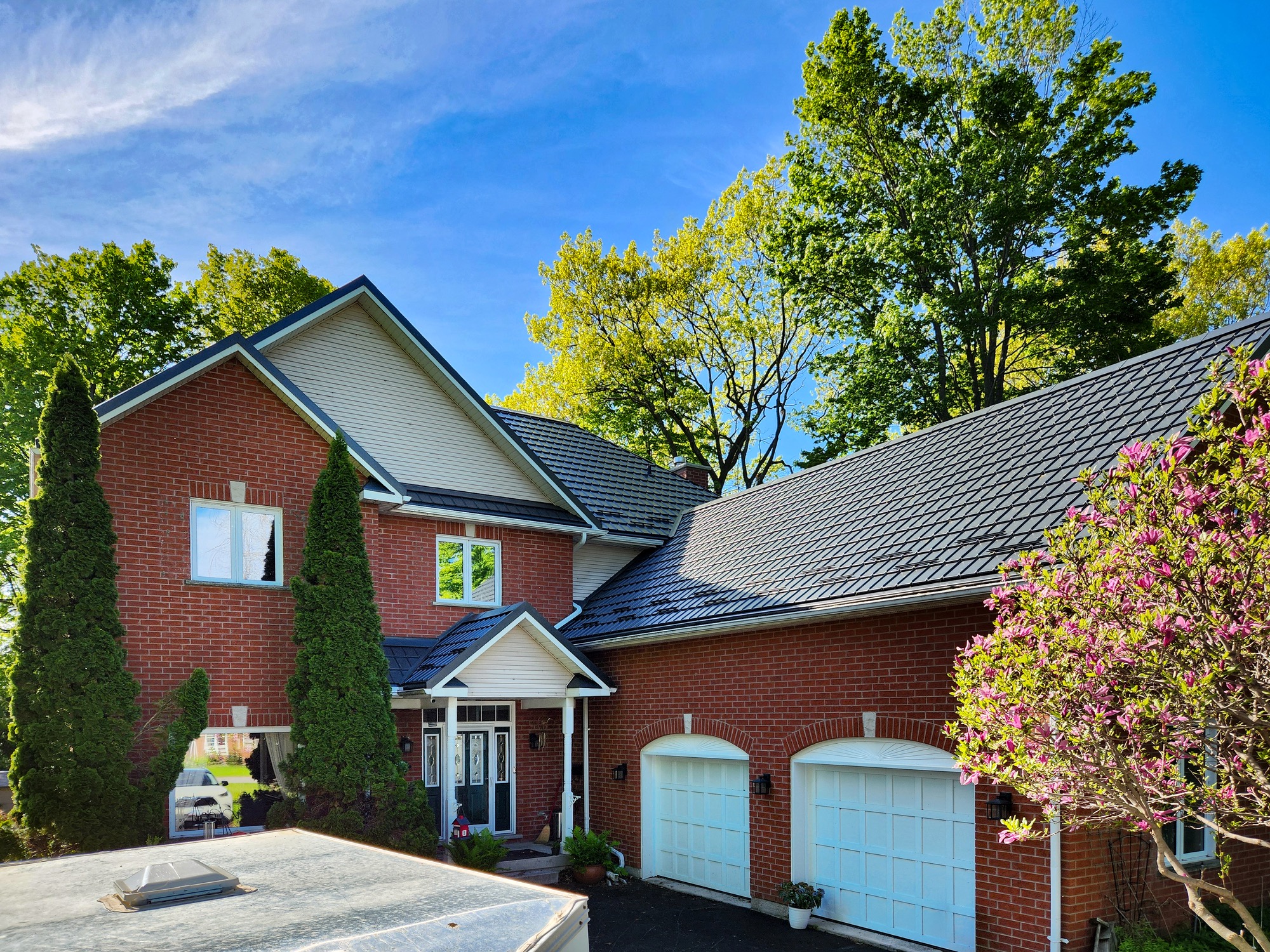 Close up of large red brick home, attached double car garage and black steel roof