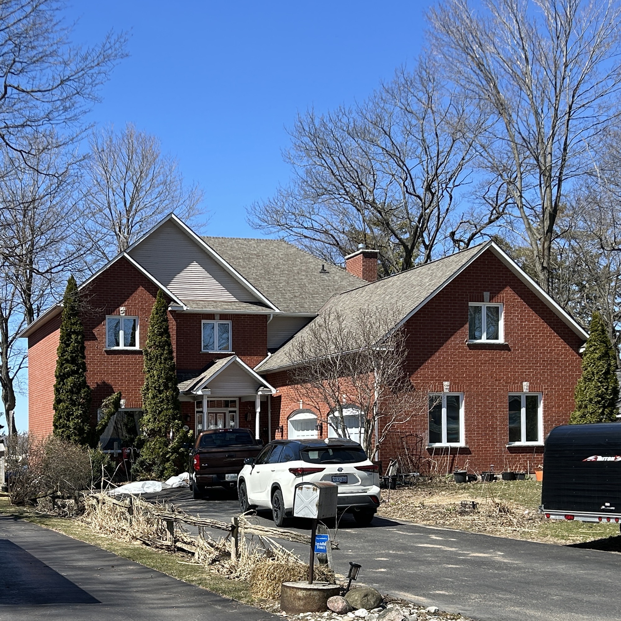 Large red brick home with shingled roof and white car in driveway
