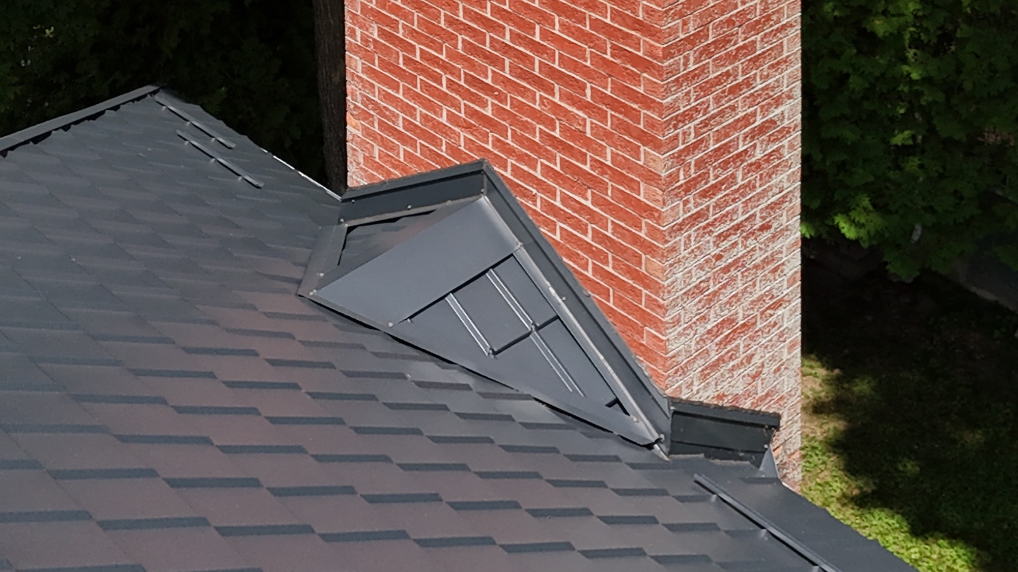 Close up of back steel roof on red brick home, where it connects at chimney