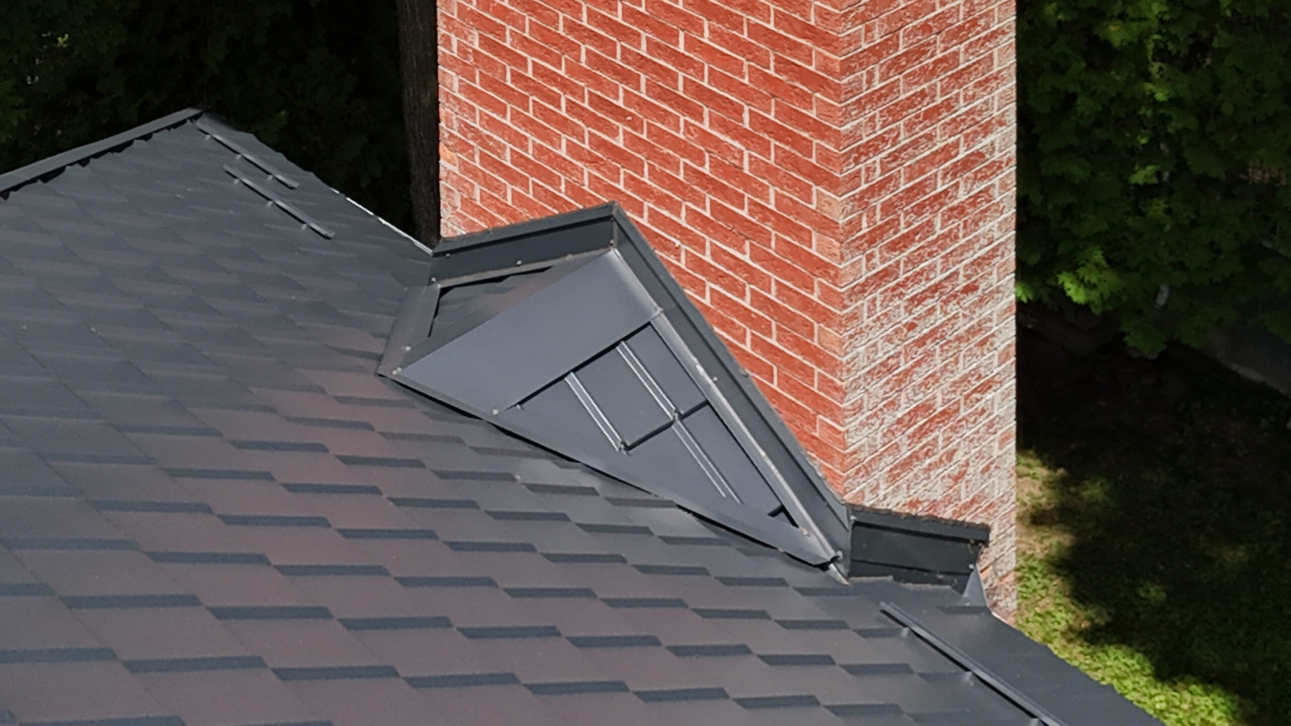 Close up of back steel roof on red brick home, where it connects at chimney